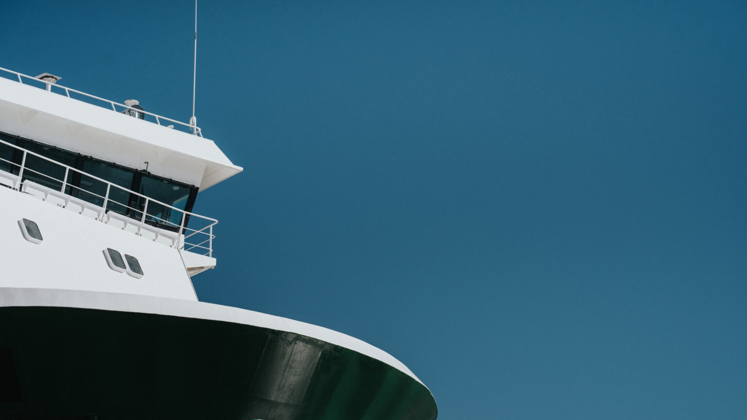 Close-up of a white ship’s bridge and deck against a clear blue sky.